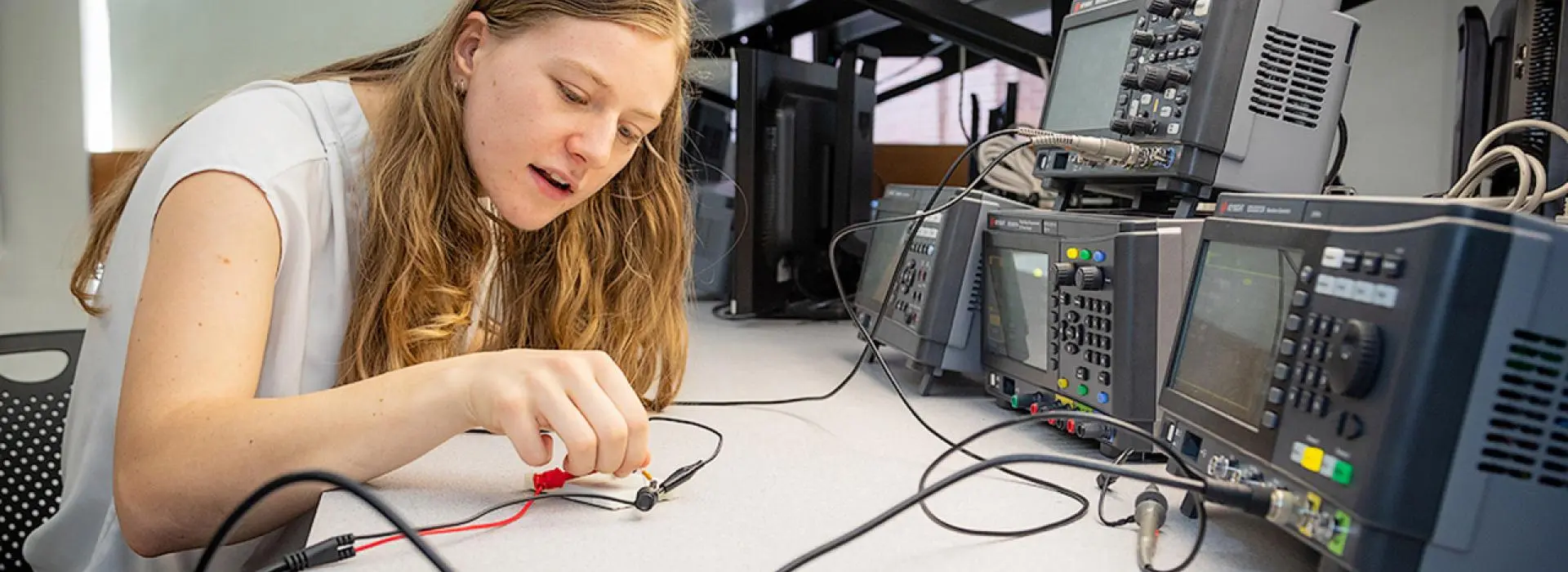 A student sitting at a workstation adjusting electrical testing and measurement equipment.