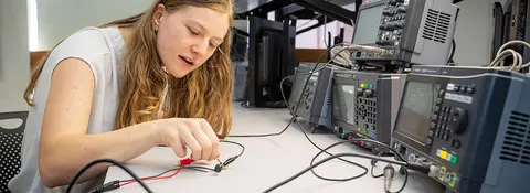 A student sitting at a workstation adjusting electrical testing and measurement equipment.