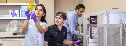 Graduate students Lakshmi Prakasan (left) and Jacob Manzi (center) under the supervision of Assoc. Prof. Harish Subbaraman (right) examine a self-sintered printed gold pattern printed on a flexible substrate using a Space Foundry plasma-jet printer.